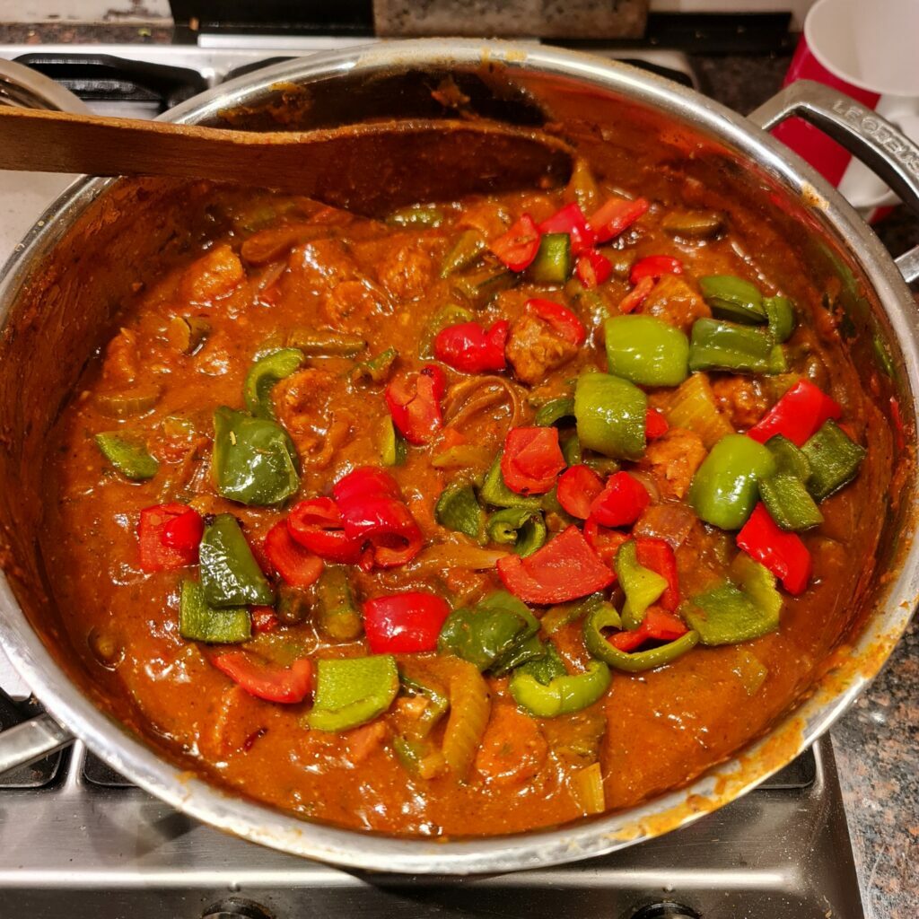 adding the red and green sauteed peppers to the gumbo